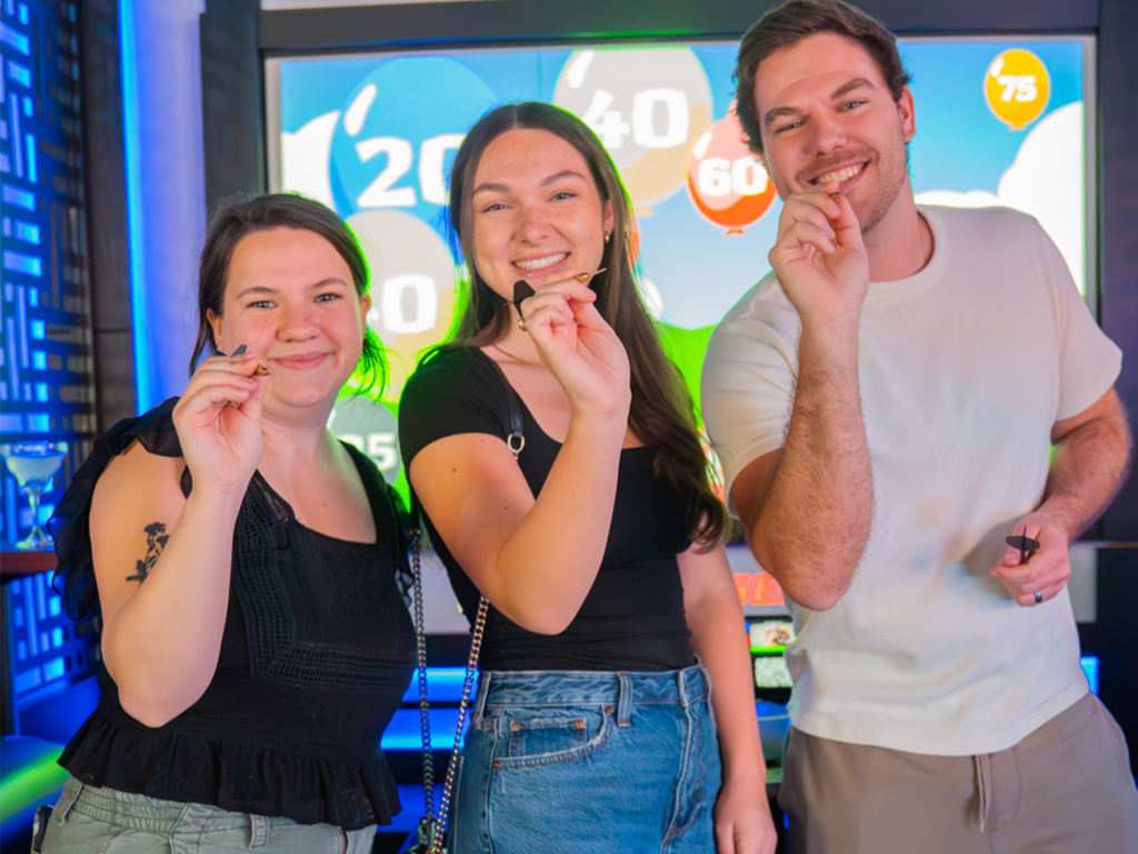 young adults smiling and holding darts